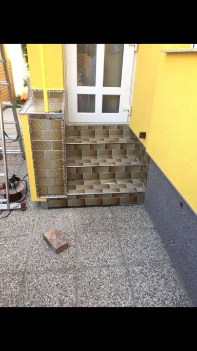 Treppen mit hellen Fliesen und gelber Wand, daneben eine Leiter und ein Ziegelstein.