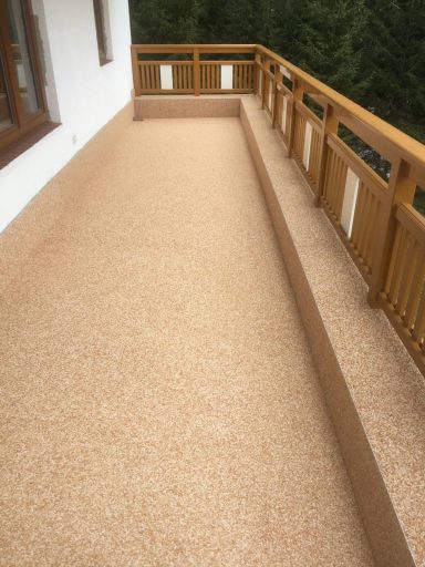 Balkon mit hellem Belag und Holzgeländer, umgeben von Bäumen.